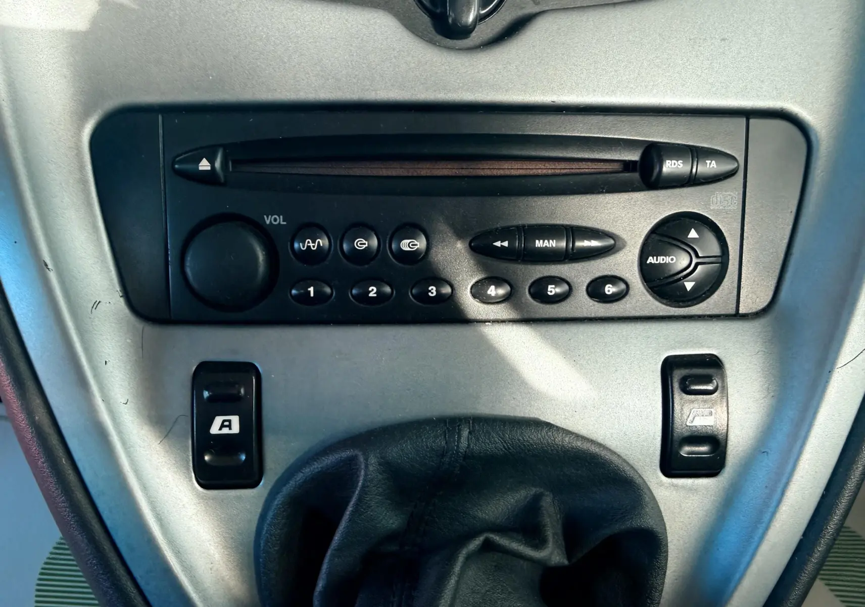 Vue rapprochée de la console centrale grise avec autoradio et levier de vitesse en cuir noir d'une Citroën Xsara Picasso beige.