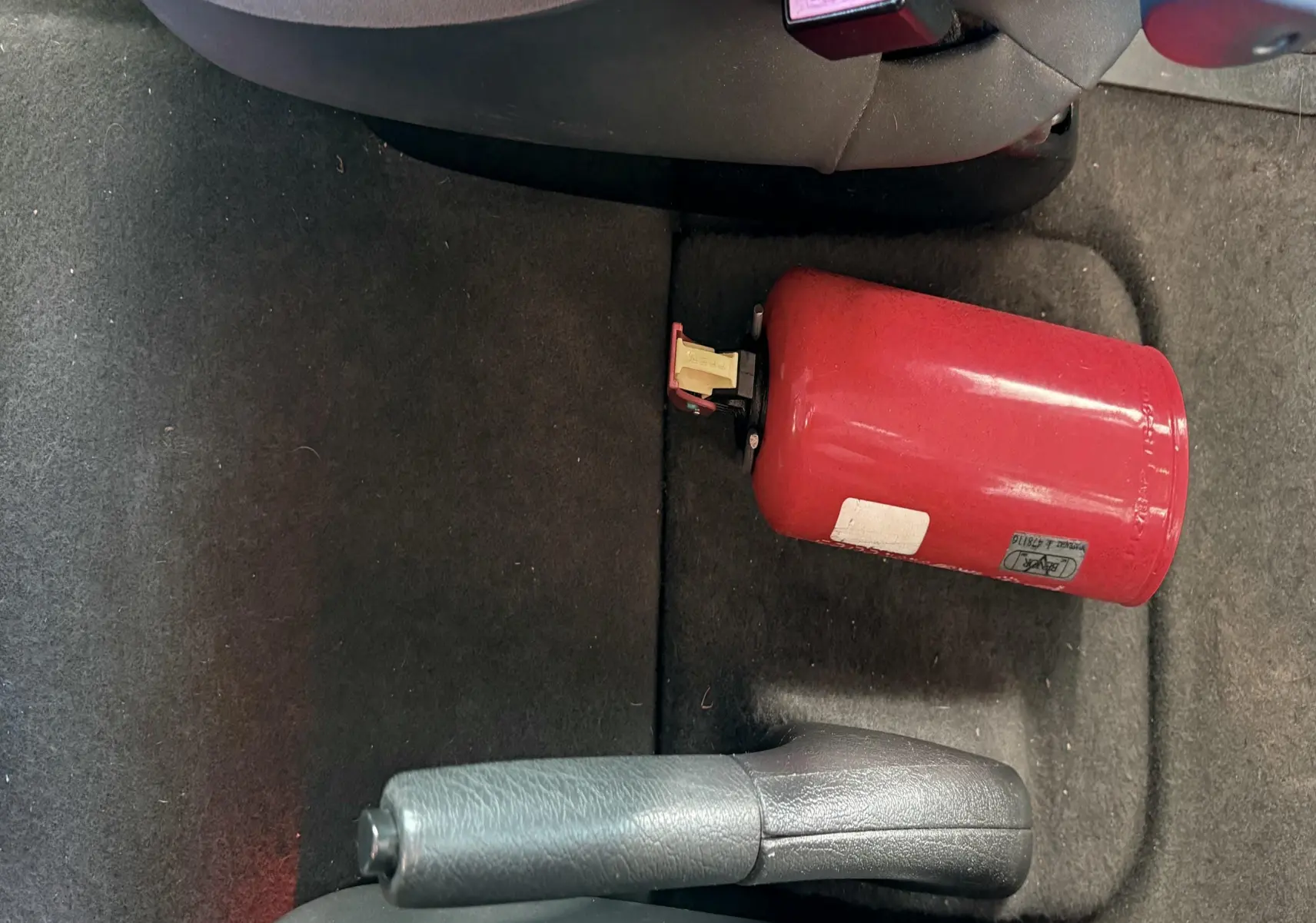 Vue rapprochée de l'intérieur arrière d'une Citroën Xsara Picasso beige, montrant le frein à main et un extincteur rouge au sol.