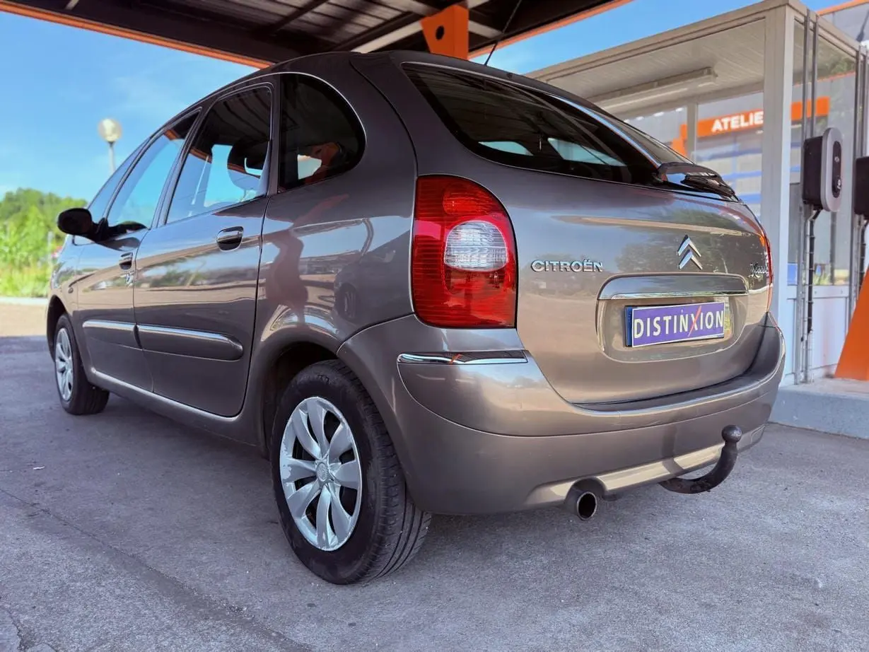 Vue 3/4 arrière droite d'une Citroën Xsara Picasso beige de 2009 avec attelage sous un auvent.