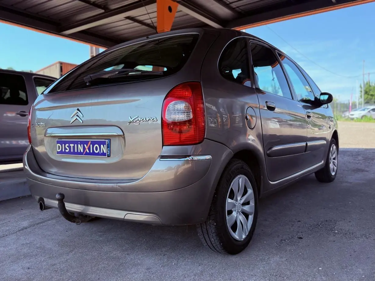 Vue 3/4 arrière droite d'une Citroën Xsara Picasso beige 2009 avec attelage sous un abri.