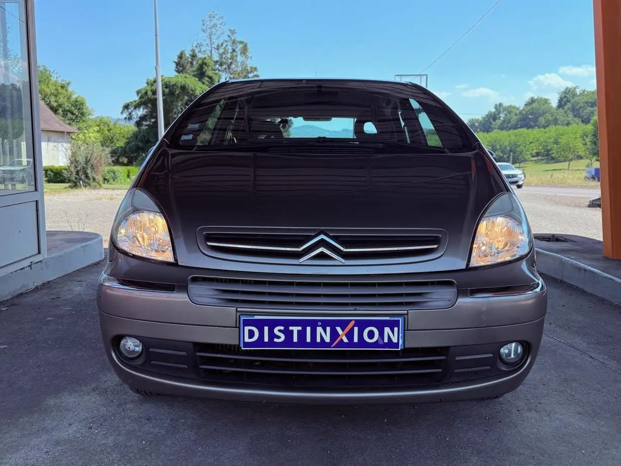 Vue avant d'une Citroën Xsara Picasso beige de 2009 avec phares allumés et plaque Distinxion visible.