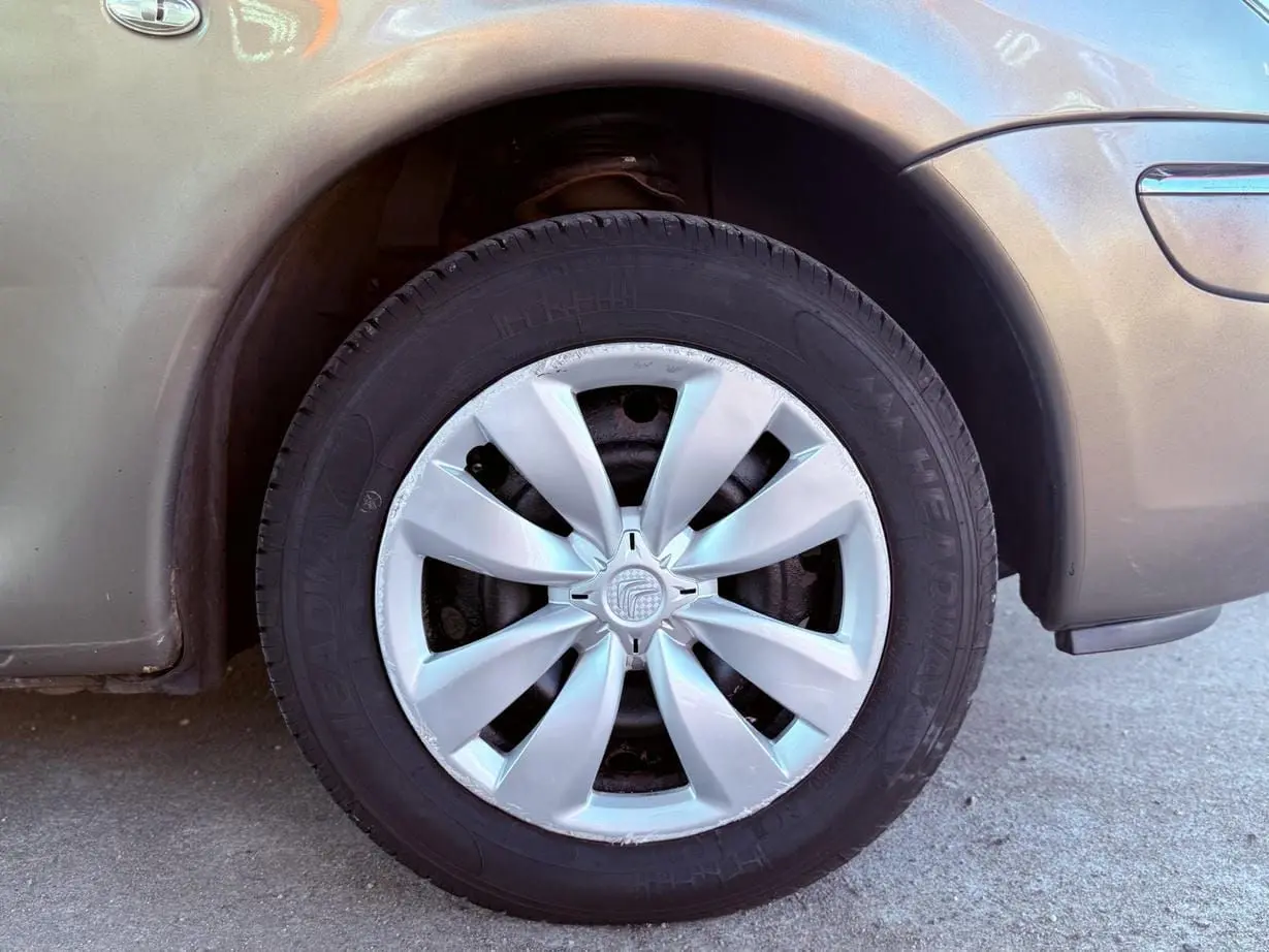 Gros plan sur la roue avant droite beige d'une Citroën Xsara Picasso avec enjoliveur argenté en extérieur.