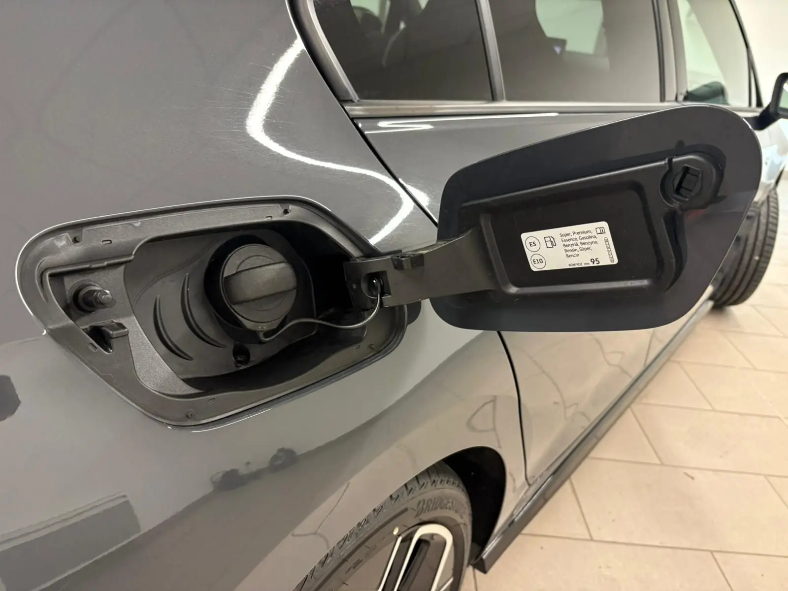 Gros plan sur la trappe à carburant ouverte côté gauche d'une Volkswagen Golf gris dauphin 2025.