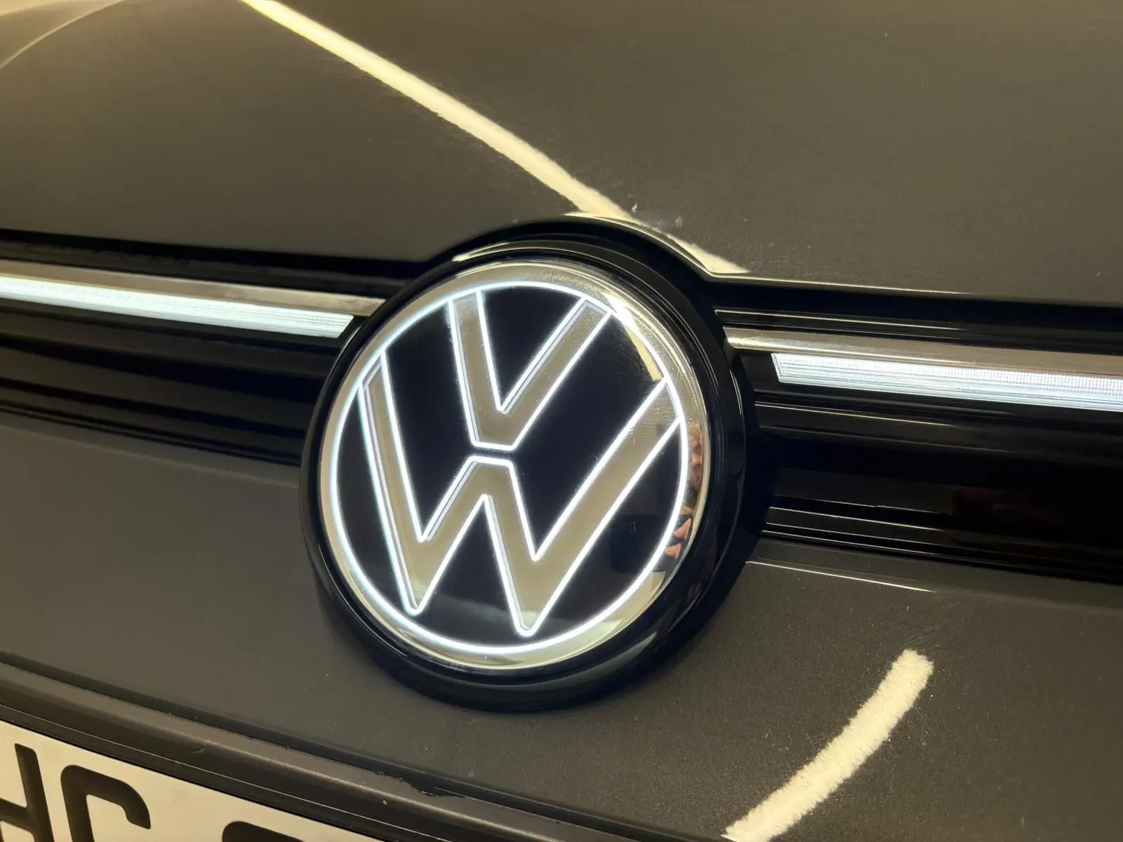 Gros plan sur le logo Volkswagen éclairé sur la calandre d'une Golf 1.5 eTSI gris dauphin, vue avant.