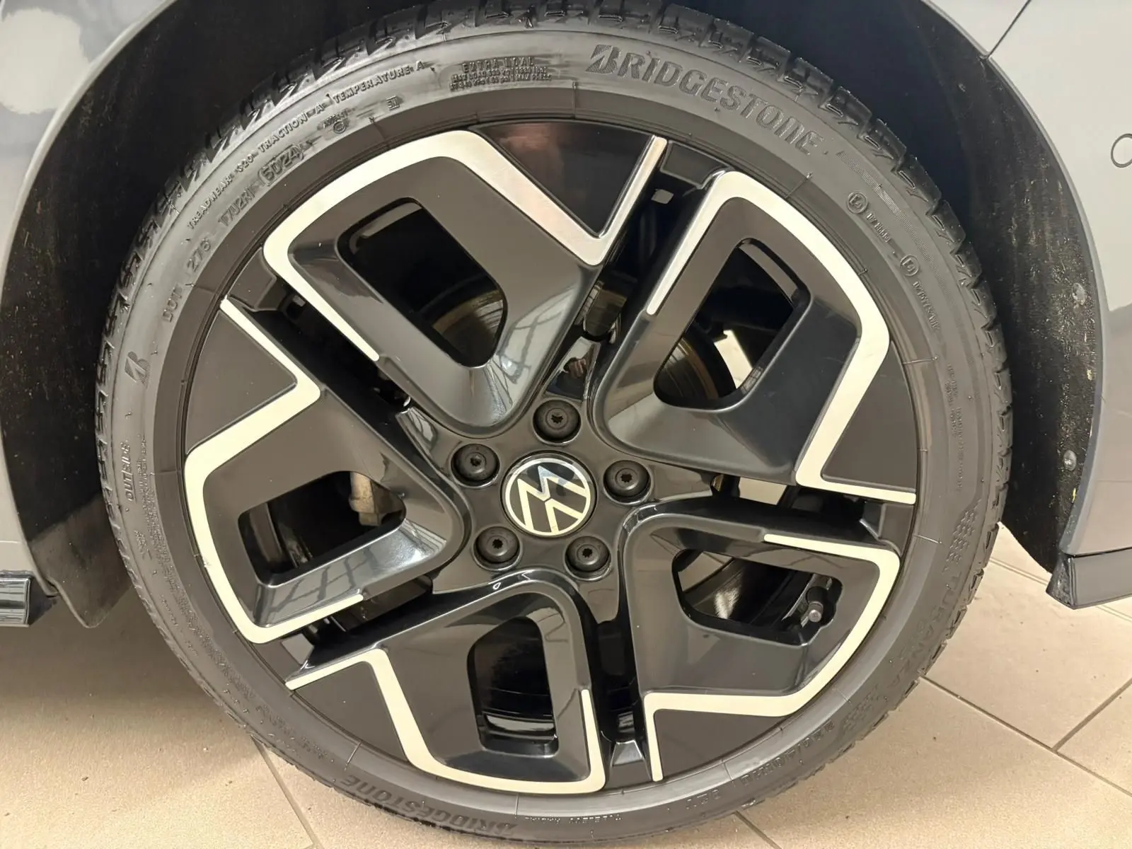 Gros plan sur la jante noire et argentée d'une Volkswagen Golf Gris Dauphin, mettant en valeur le logo VW central.