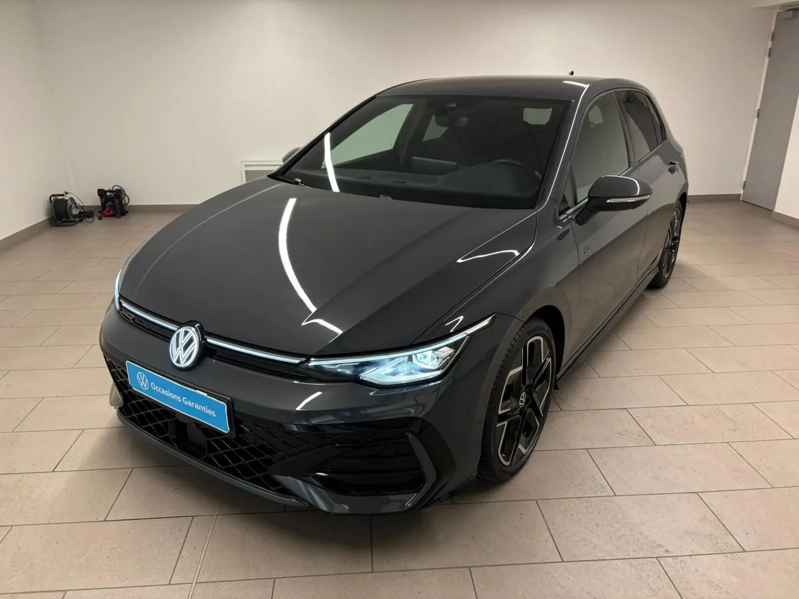 Volkswagen Golf 1.5 eTSI R-Line Gris Dauphin vue 3/4 avant droit en intérieur avec phares allumés.