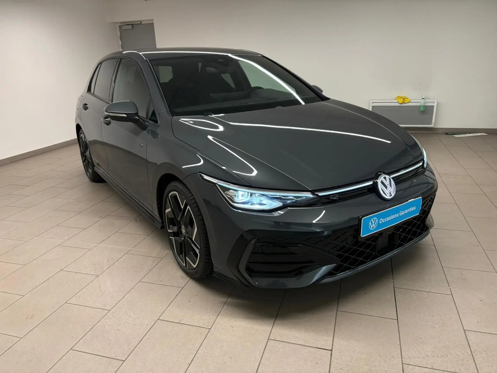 Volkswagen Golf 1.5 eTSI R-Line gris dauphin vue 3/4 avant droit avec phares LED allumés en intérieur.