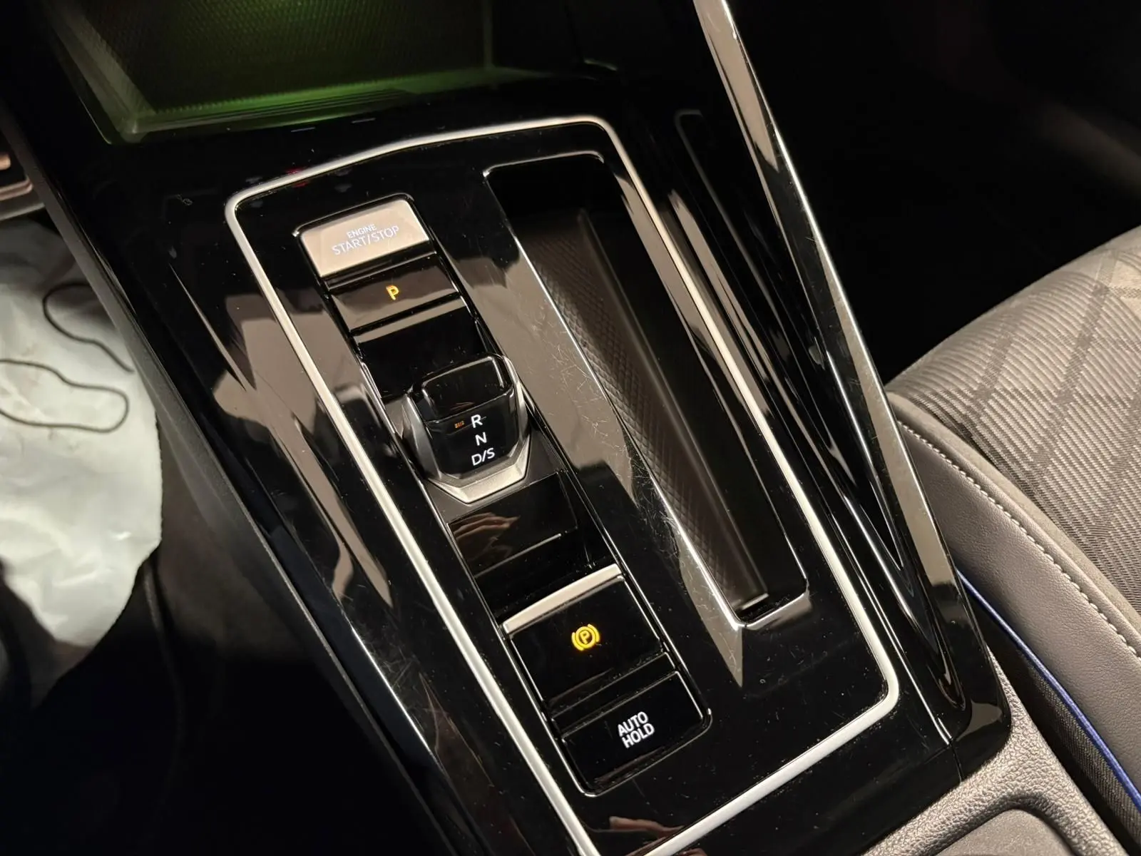 Gros plan sur la console centrale noire brillante de la Volkswagen Golf 1.5 eTSI 2025 avec levier de vitesses automatique et bouton start/stop.