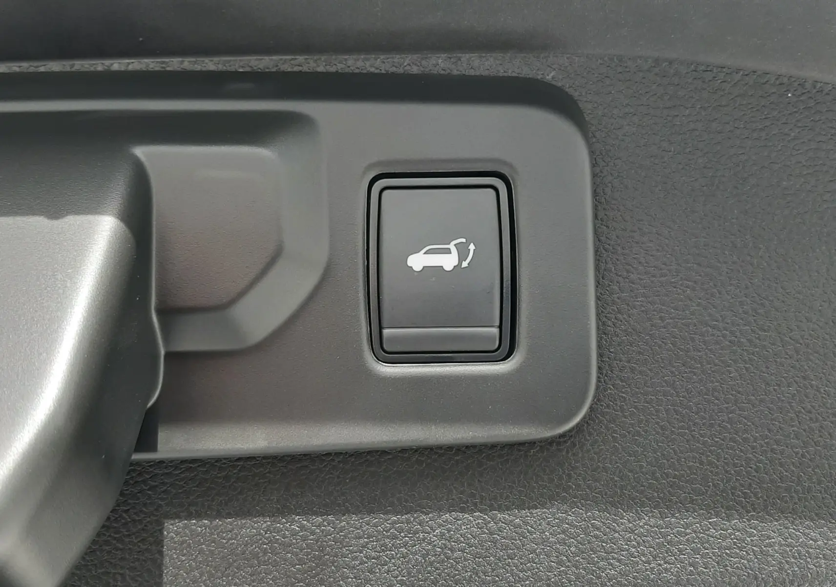 Bouton d'ouverture électrique du hayon sur la garniture intérieure d'un Renault Austral blanc nacré.