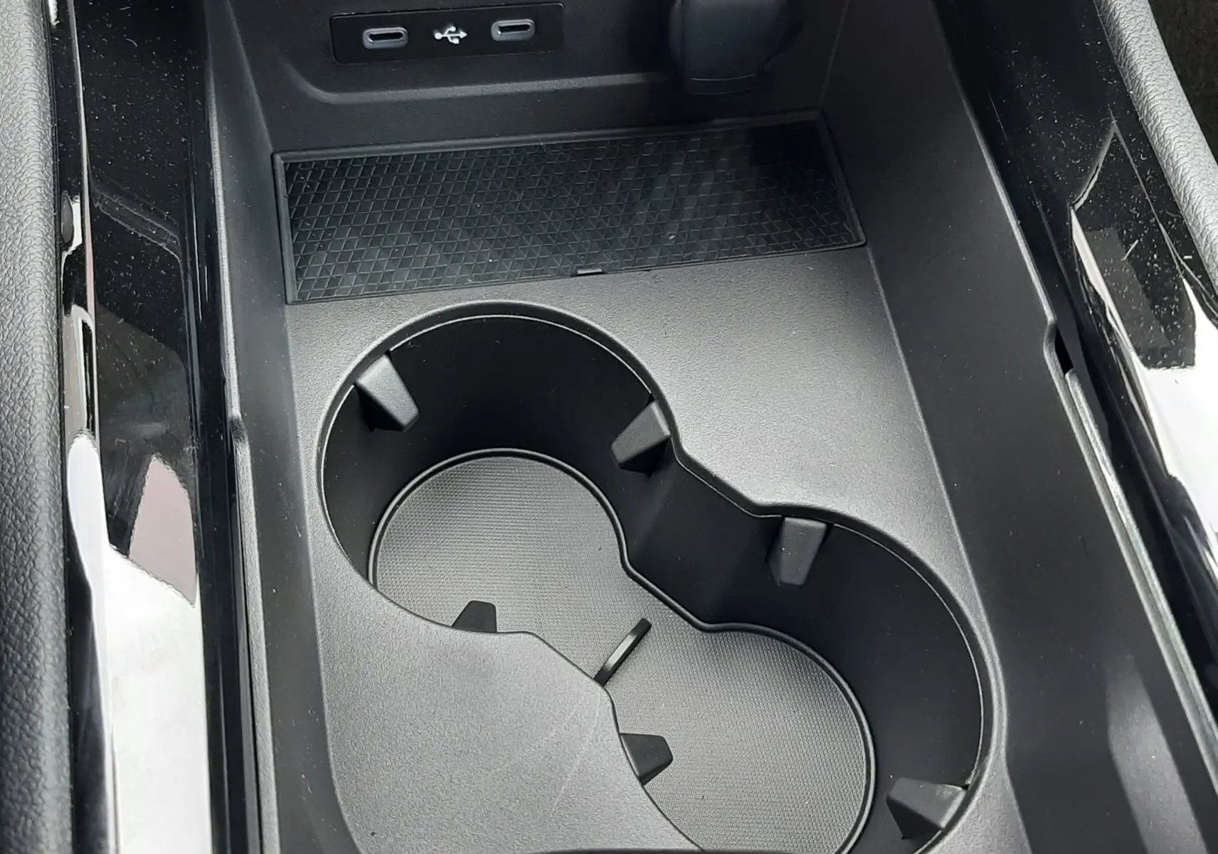 Gros plan sur la console centrale noire du Renault Austral avec porte-gobelets et ports USB visibles.