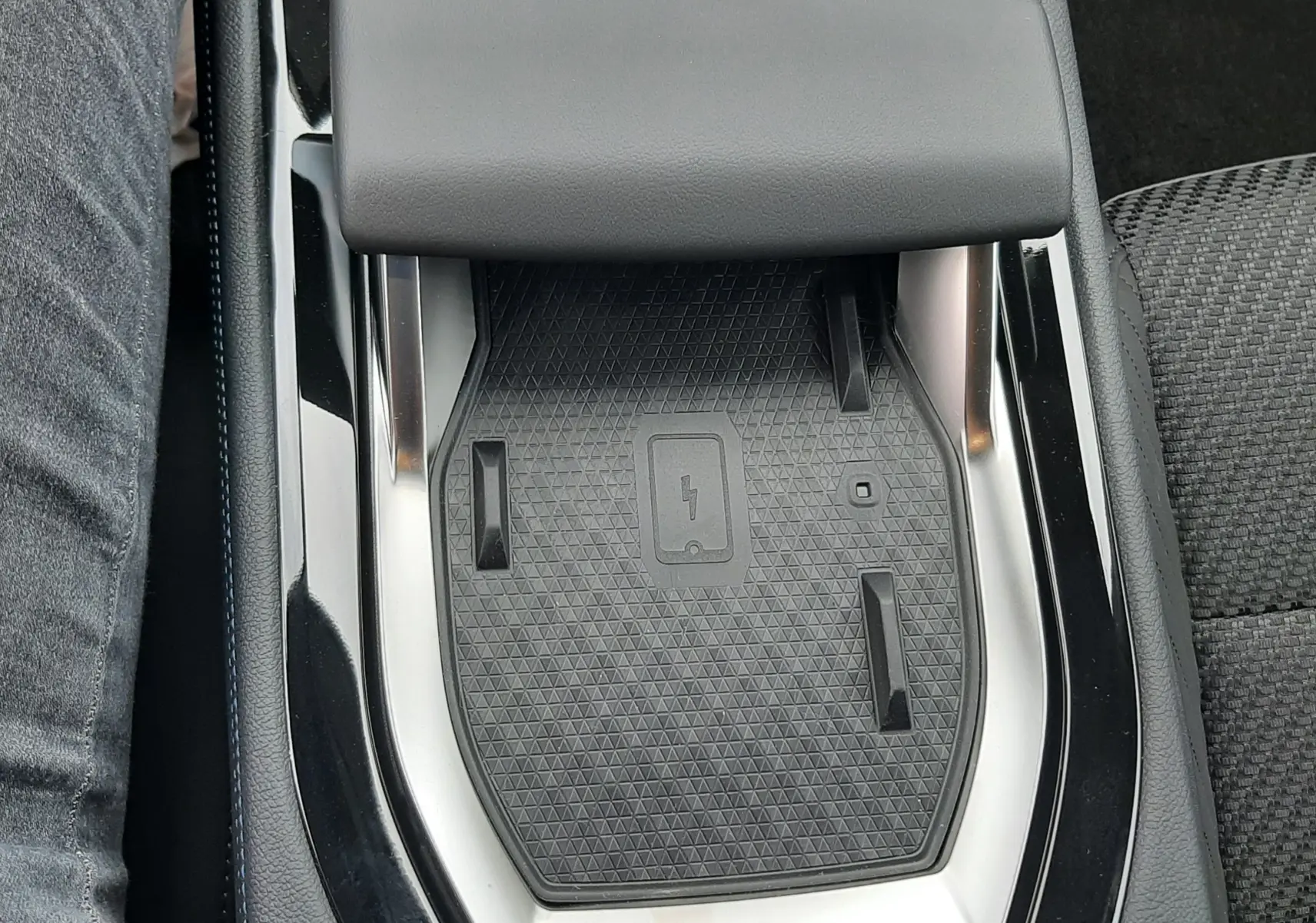Vue plongeante sur la console centrale noire du Renault Austral hybride, mettant en valeur le chargeur à induction et l'accoudoir gris.