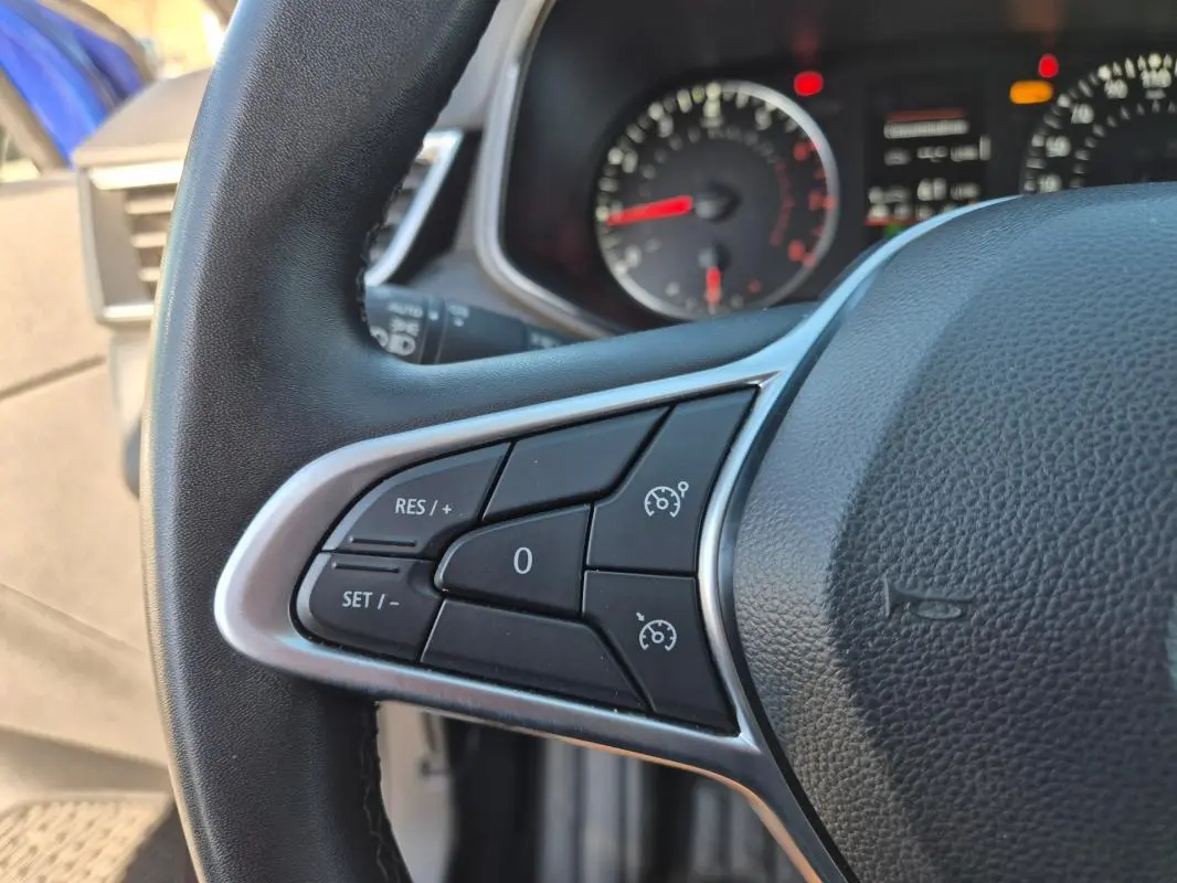 Gros plan sur le volant de la Renault Clio bleu foncé 2023, montrant les commandes du régulateur de vitesse côté gauche.