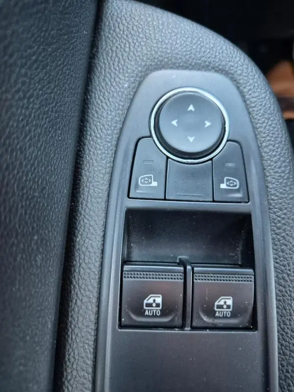 Gros plan sur les commandes de lève-vitres et réglage des rétroviseurs intérieurs d'une Renault Clio bleu foncé 2023.