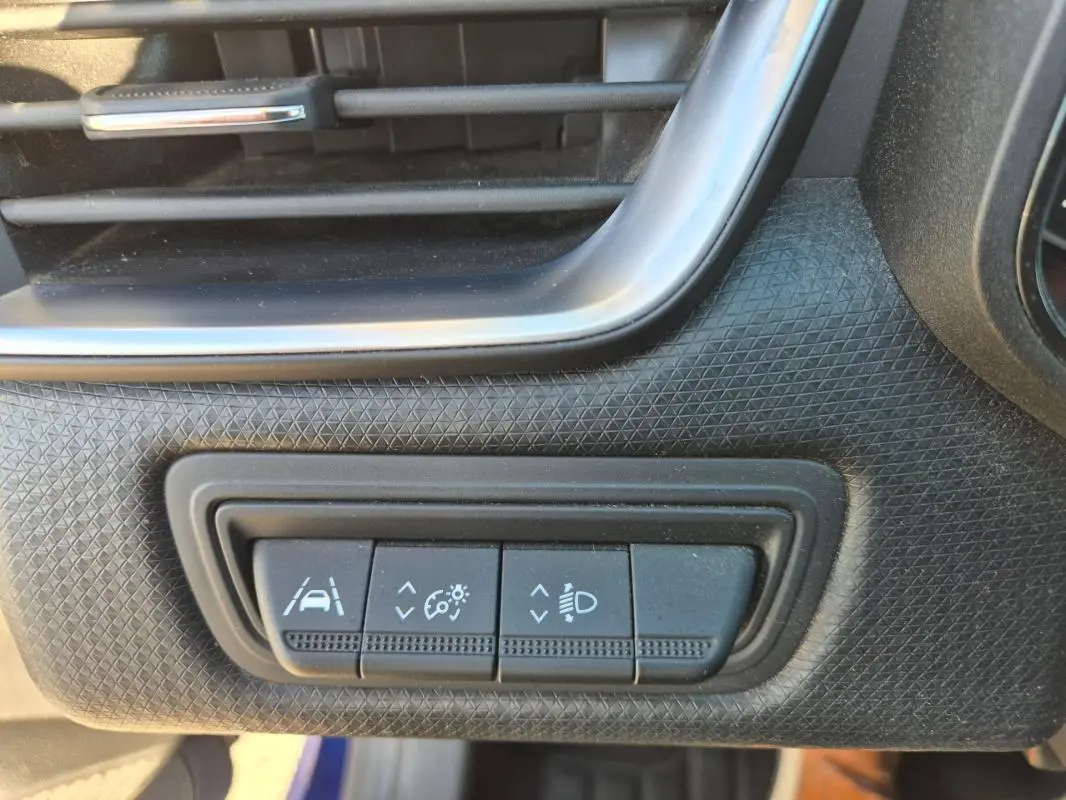 Détail intérieur montrant les commandes d'assistance à la conduite sur tableau de bord noir d'une Renault Clio bleu foncé.