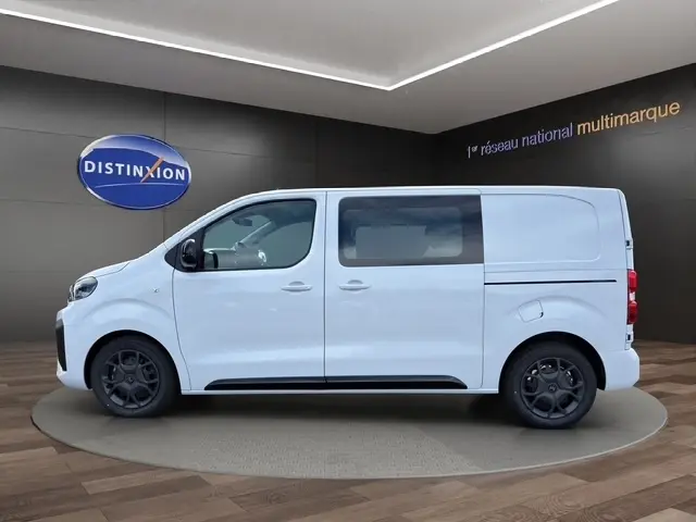 Vue latérale droite d'un Citroën Jumpy blanc 2026 avec vitres teintées et jantes noires en intérieur showroom.