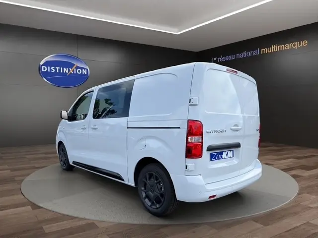Vue 3/4 arrière droite d’un Citroën Jumpy blanc, fourgon avec vitres latérales et jantes noires, en showroom.