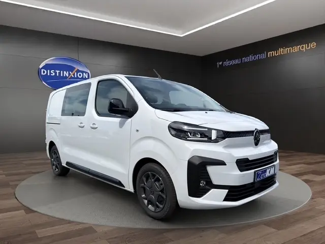 Vue 3/4 avant droite d'un Citroën Jumpy blanc avec jantes noires et vitres latérales teintées dans un showroom.