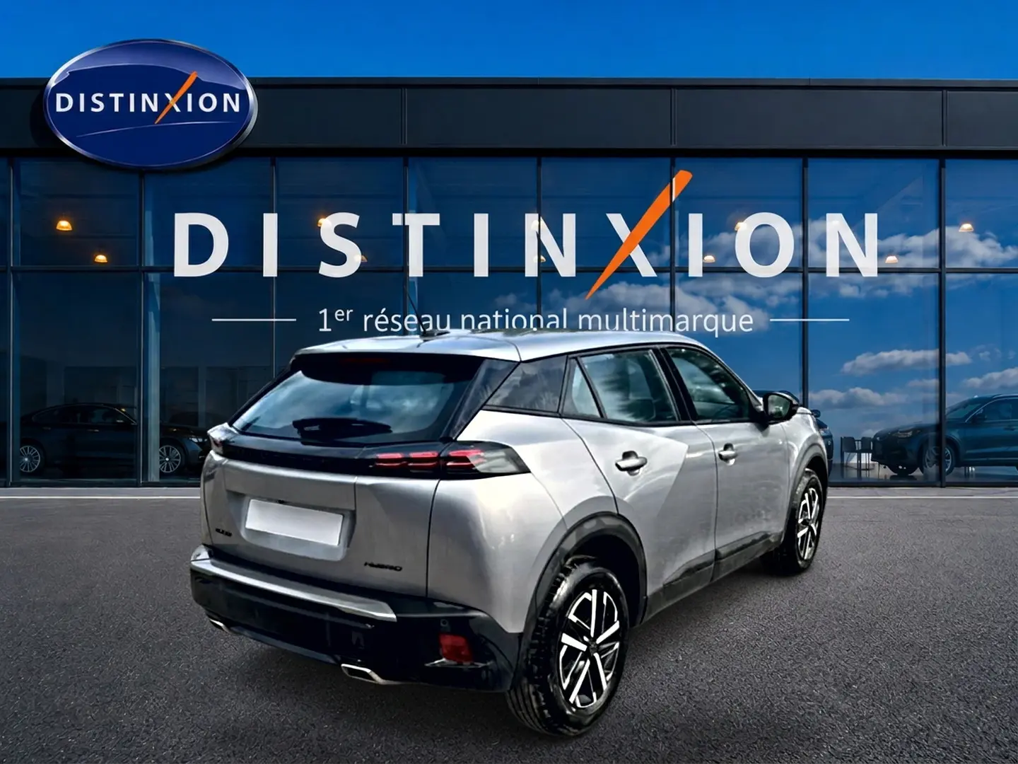 Peugeot 2008 gris en 3/4 arrière droit, avec becquet et feux arrière LED visibles devant un showroom Distinxion.
