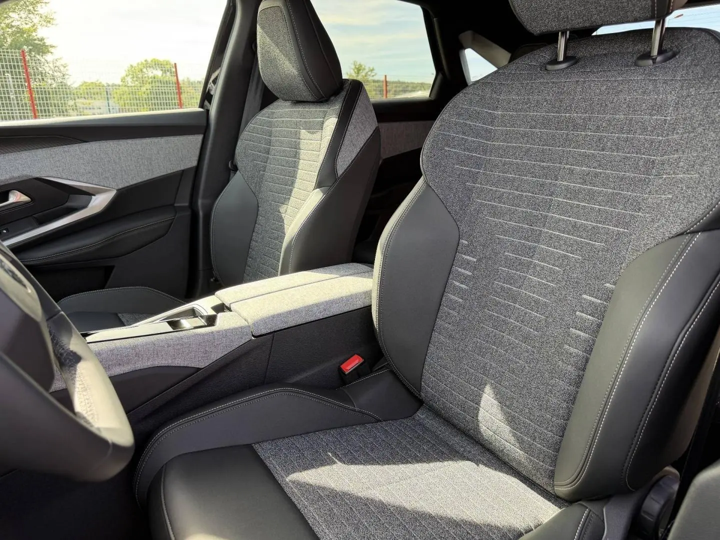 Vue intérieure rapprochée des sièges avant gris tissu et cuir noir du Peugeot 3008 Hybrid 2026, côté conducteur et passager.