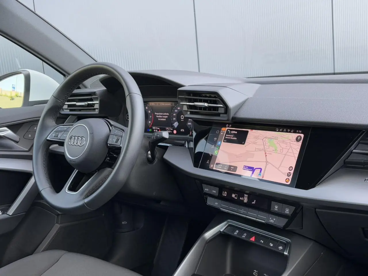 Intérieur Audi A3 Sportback 2024 vu côté gauche, tableau de bord noir avec écran tactile affichant la navigation.