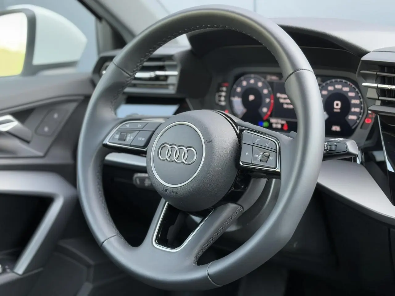 Volant cuir 3 branches multifonctions de l'Audi A3 Sportback 2024, vue rapprochée du poste de conduite intérieur.