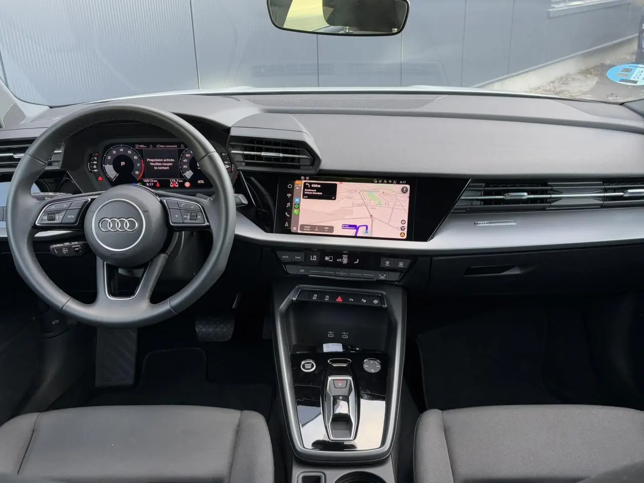 Vue intérieure frontale de l'Audi A3 Sportback 2024, tableau de bord moderne avec écran tactile et volant cuir multifonctions.
