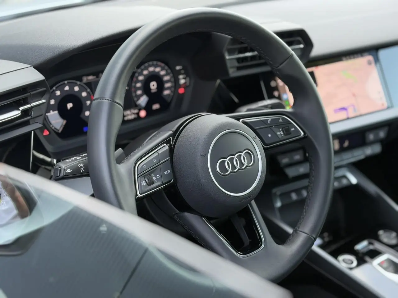 Volant cuir trois branches de l'Audi A3 Sportback 2024 vu côté conducteur avec tableau de bord numérique et écran tactile.