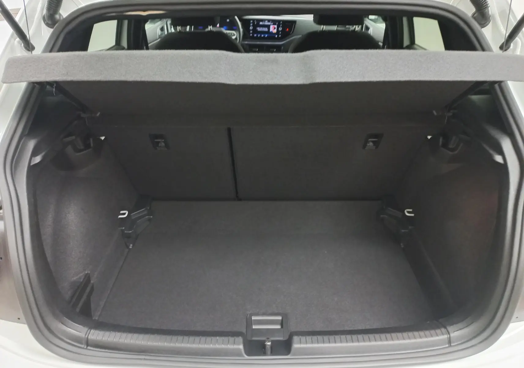 Coffre ouvert d'une Volkswagen Polo blanc pur vue de l'arrière, montrant l'espace de chargement et l'intérieur sombre.