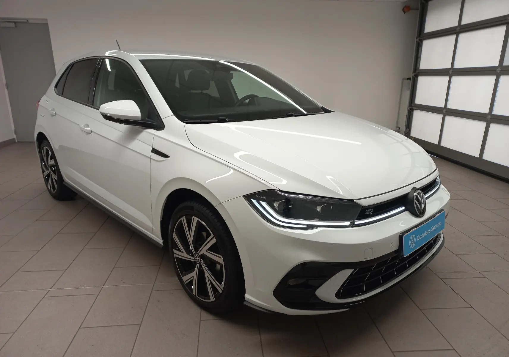Vue 3/4 avant droit d'une Volkswagen Polo blanc pur avec phares LED et jantes alliage R-Line dans un garage.