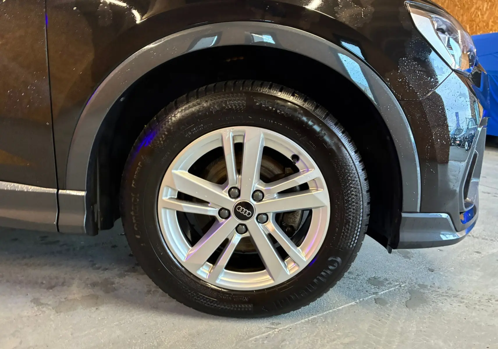 Gros plan sur la roue avant droite avec jante alu argentée d’un Audi Q3 Sportback noir 2022.