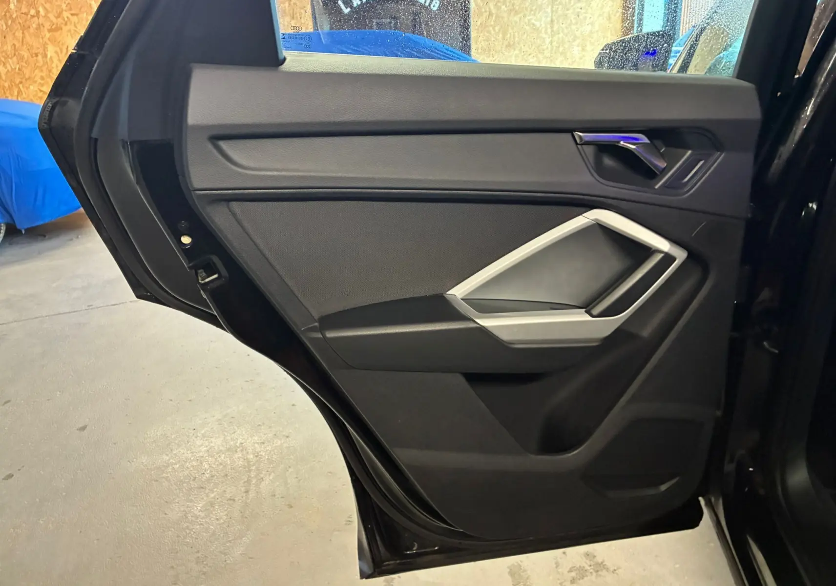 Porte arrière gauche ouverte de l'Audi Q3 Sportback noire, montrant le panneau intérieur avec poignée argentée.