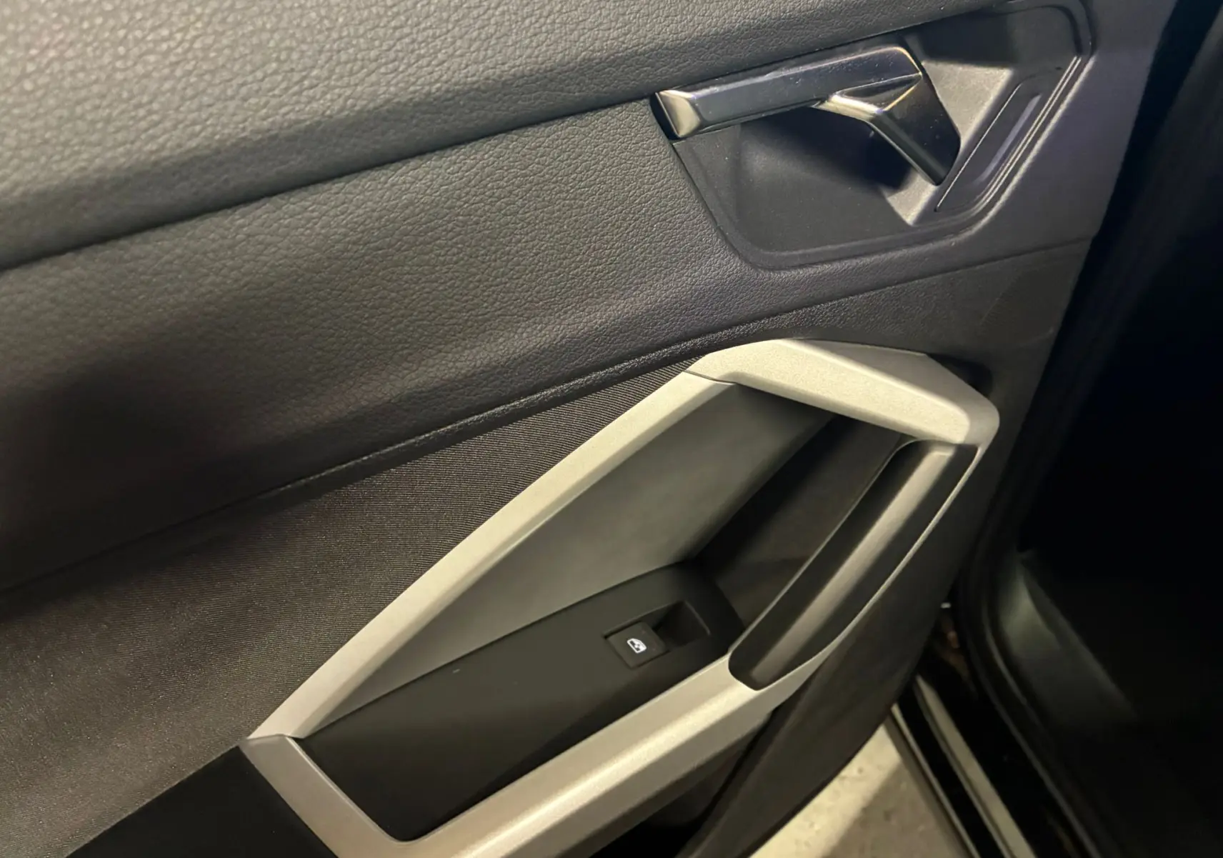 Détail de la porte intérieure côté gauche de l'Audi Q3 Sportback noire avec poignée argentée et commande de vitre électrique.