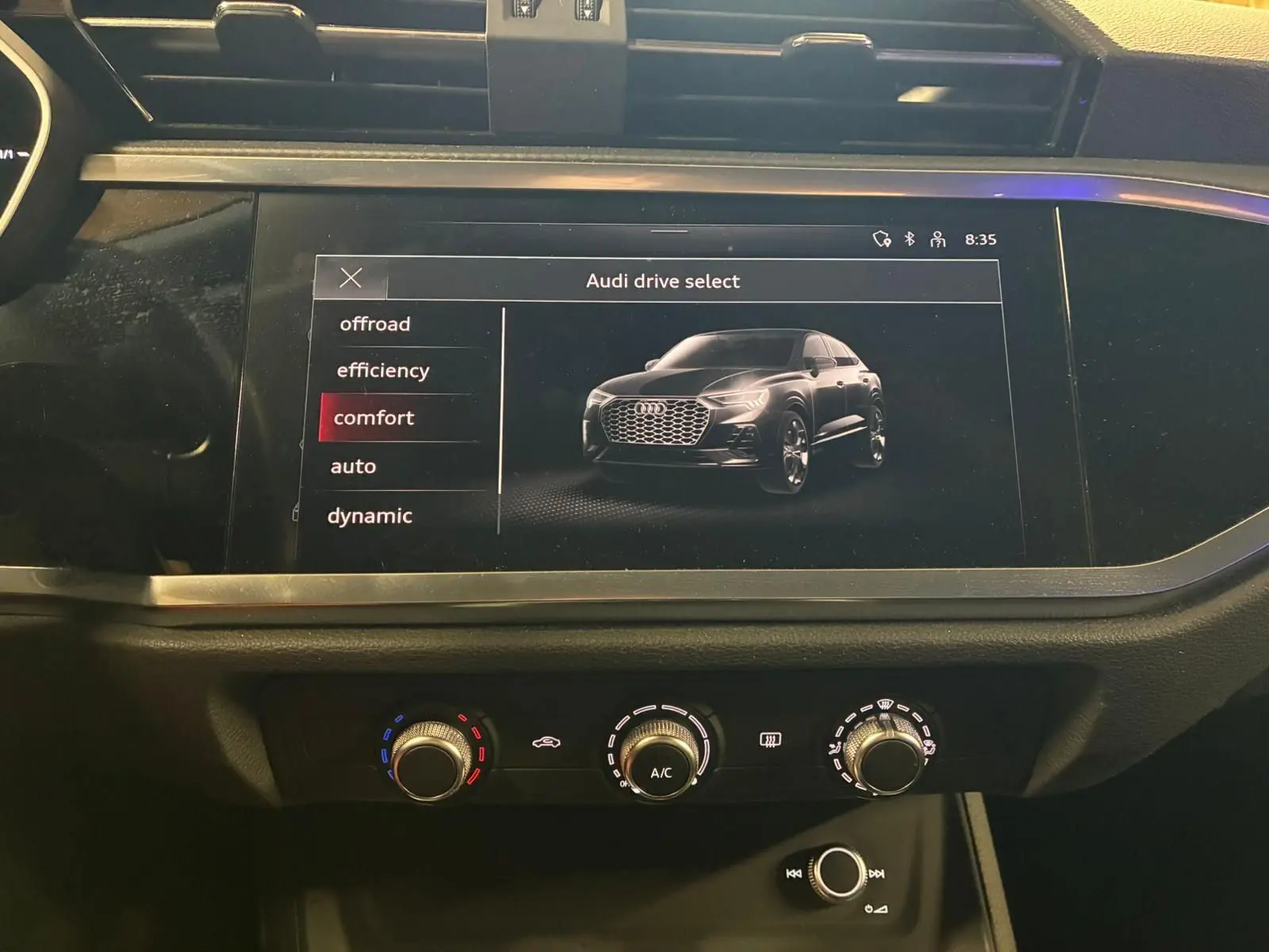 Écran tactile intérieur montrant un Audi Q3 Sportback noir en vue 3/4 avant avec menu de sélection de mode de conduite.