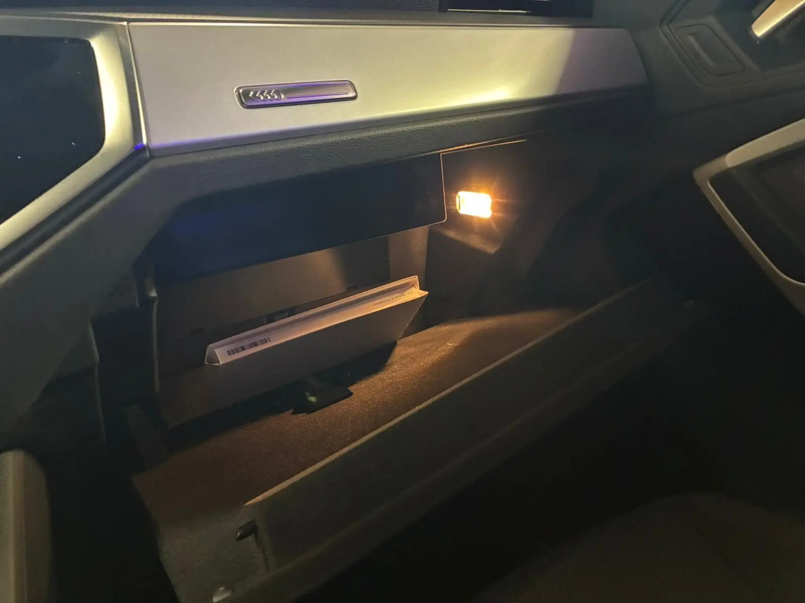 Gros plan sur la boîte à gants ouverte de l’Audi Q3 Sportback 2022 avec lumière intérieure allumée et manuel visible.