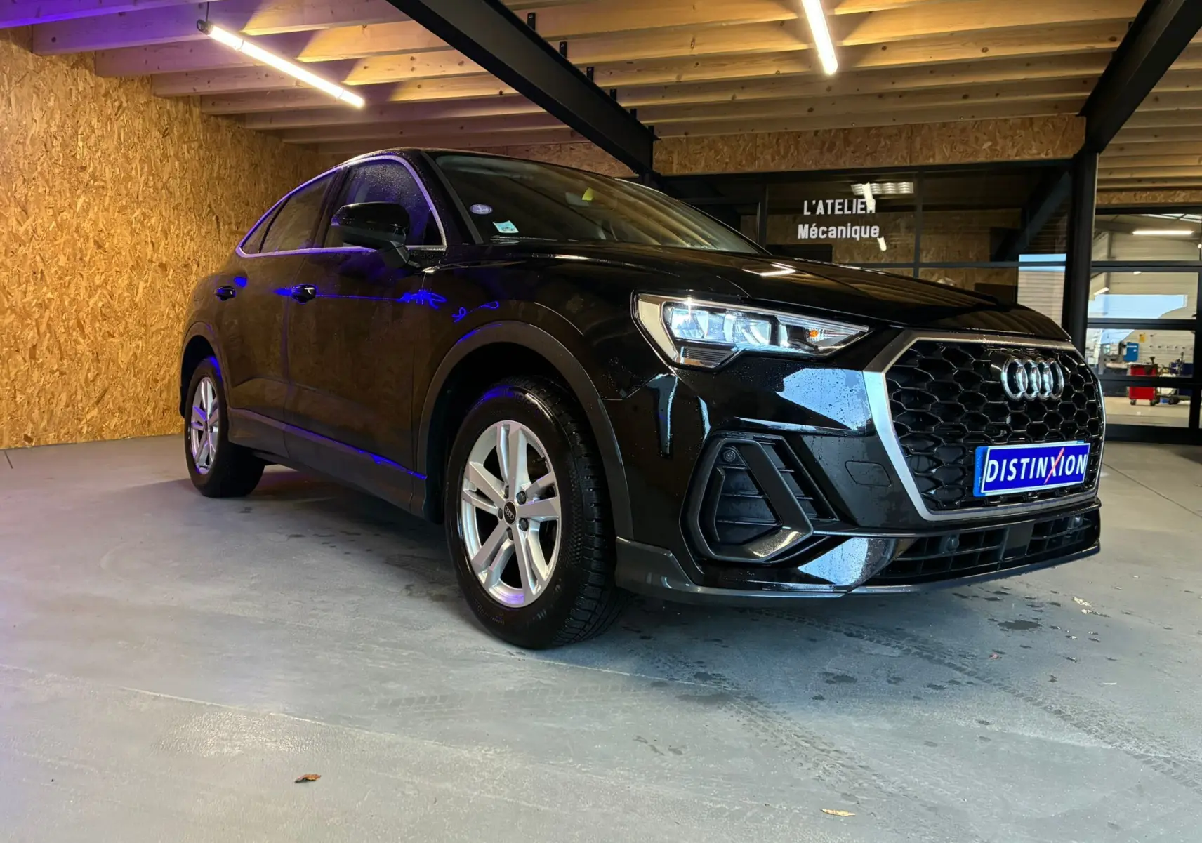Audi Q3 Sportback noir vue 3/4 avant droit, avec calandre hexagonale et jantes alu visibles en intérieur d'atelier.
