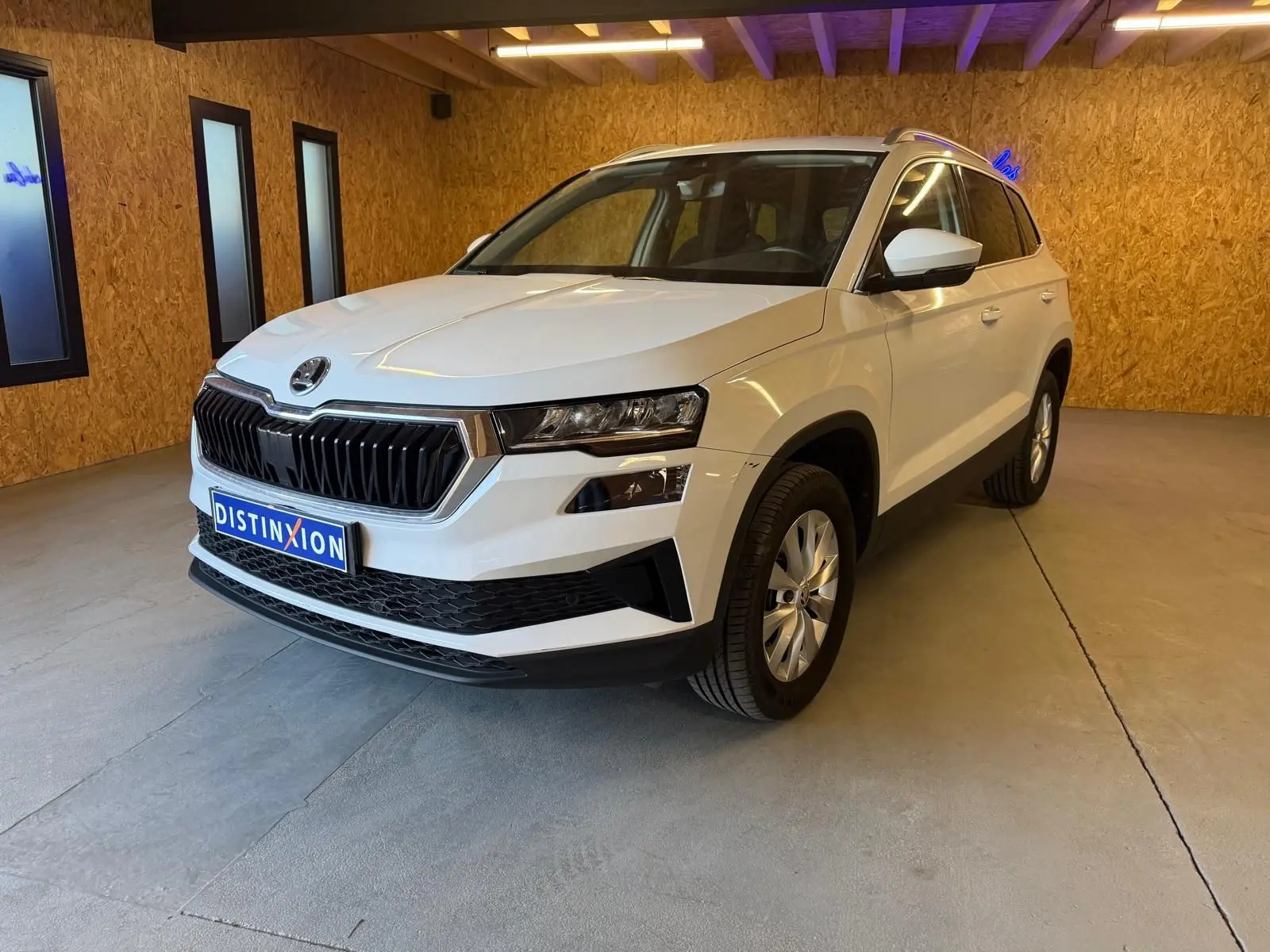 Vue 3/4 avant droite d'un Skoda Karoq blanc 2023 avec calandre noire et jantes alliage en intérieur.