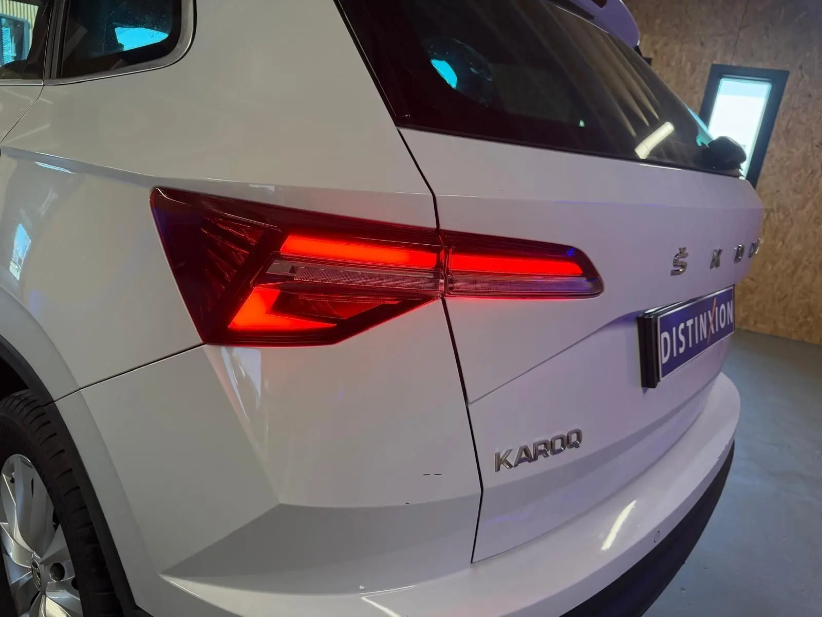 Vue 3/4 arrière droite d'un Skoda Karoq blanc 2023 avec feux arrière allumés et logo distinctif sur le hayon.
