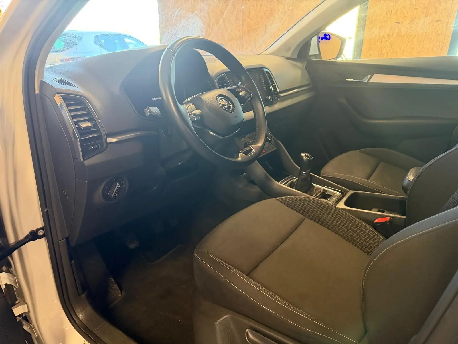 Intérieur du Skoda Karoq 2023 blanc, vue côté conducteur montrant le volant, tableau de bord et boîte manuelle.