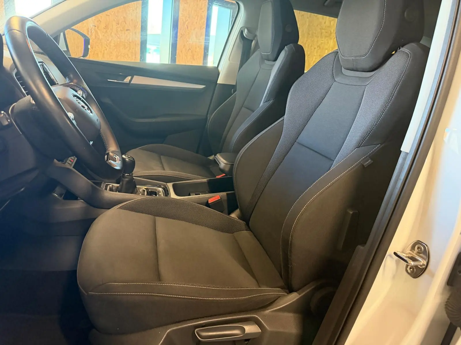 Vue intérieure côté conducteur du Skoda Karoq blanc 2023, mettant en valeur les sièges noirs et la boîte manuelle.