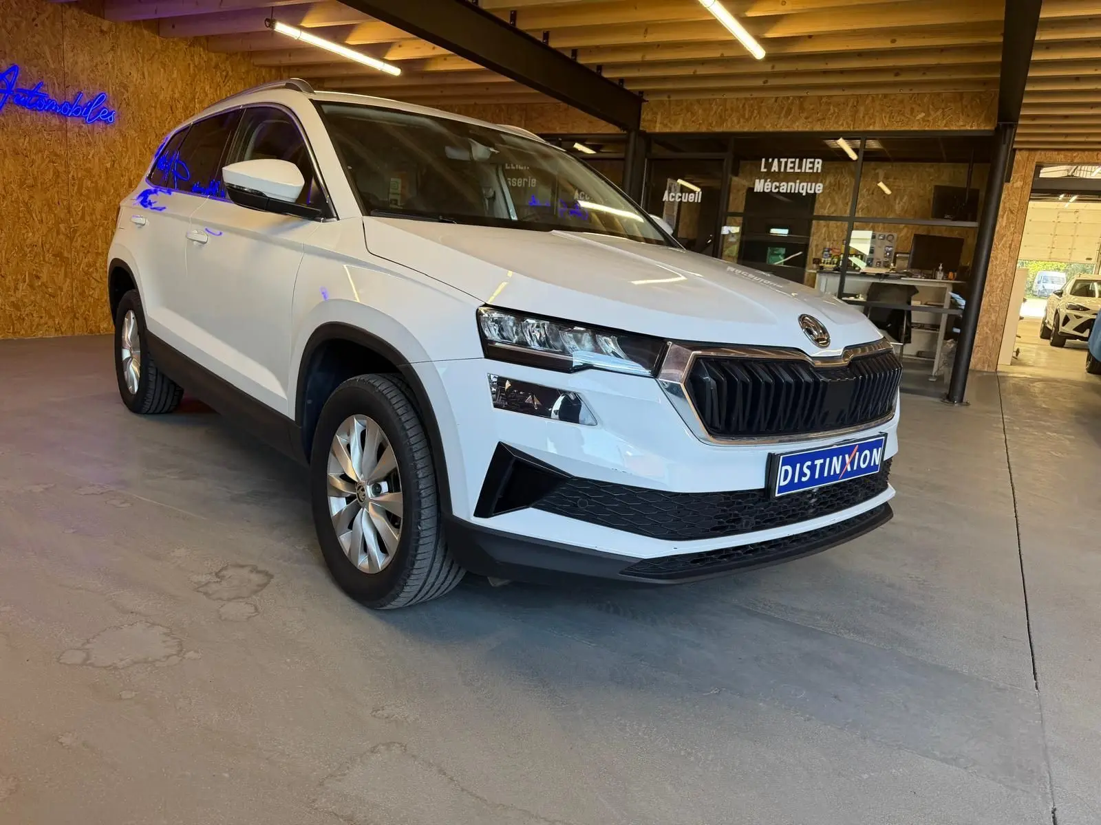 SUV Skoda Karoq blanc 2023 en 3/4 avant droit, avec calandre noire et jantes alliage visibles en intérieur showroom.
