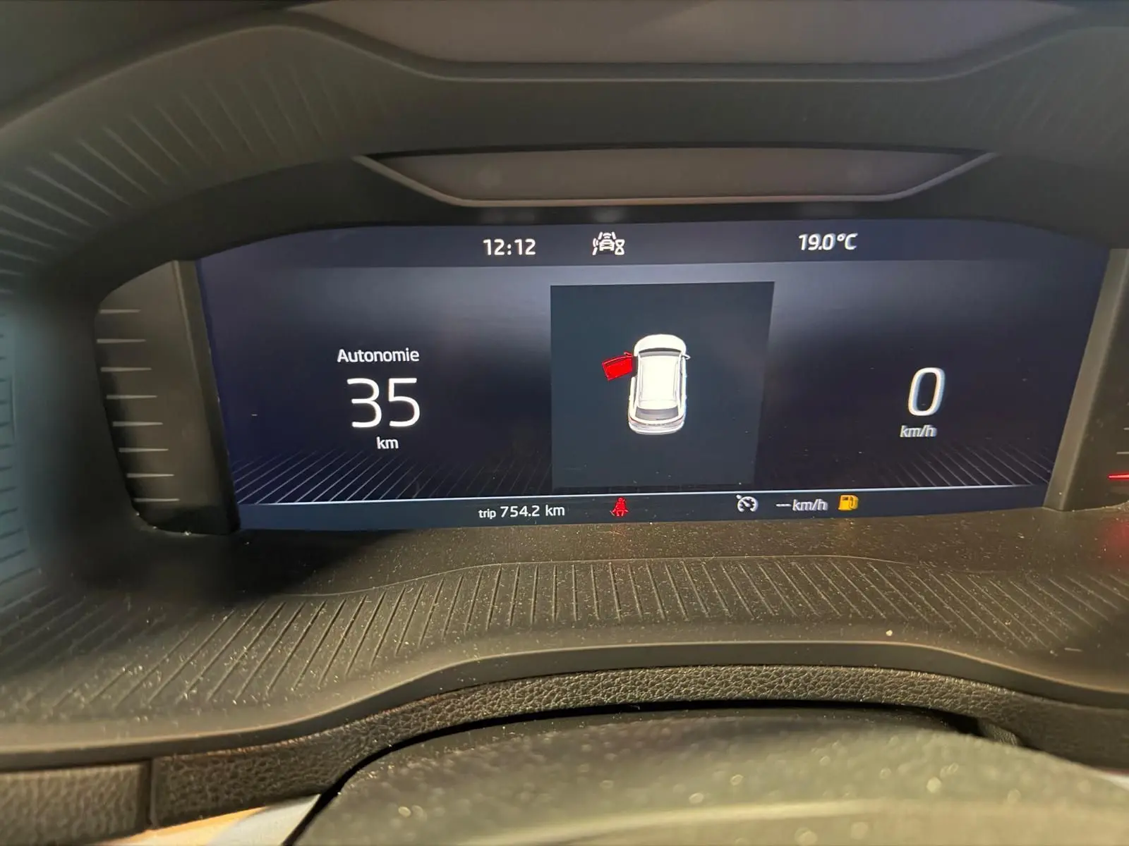 Affichage numérique du tableau de bord du Skoda Karoq blanc, montrant l'autonomie restante et la porte avant gauche ouverte.