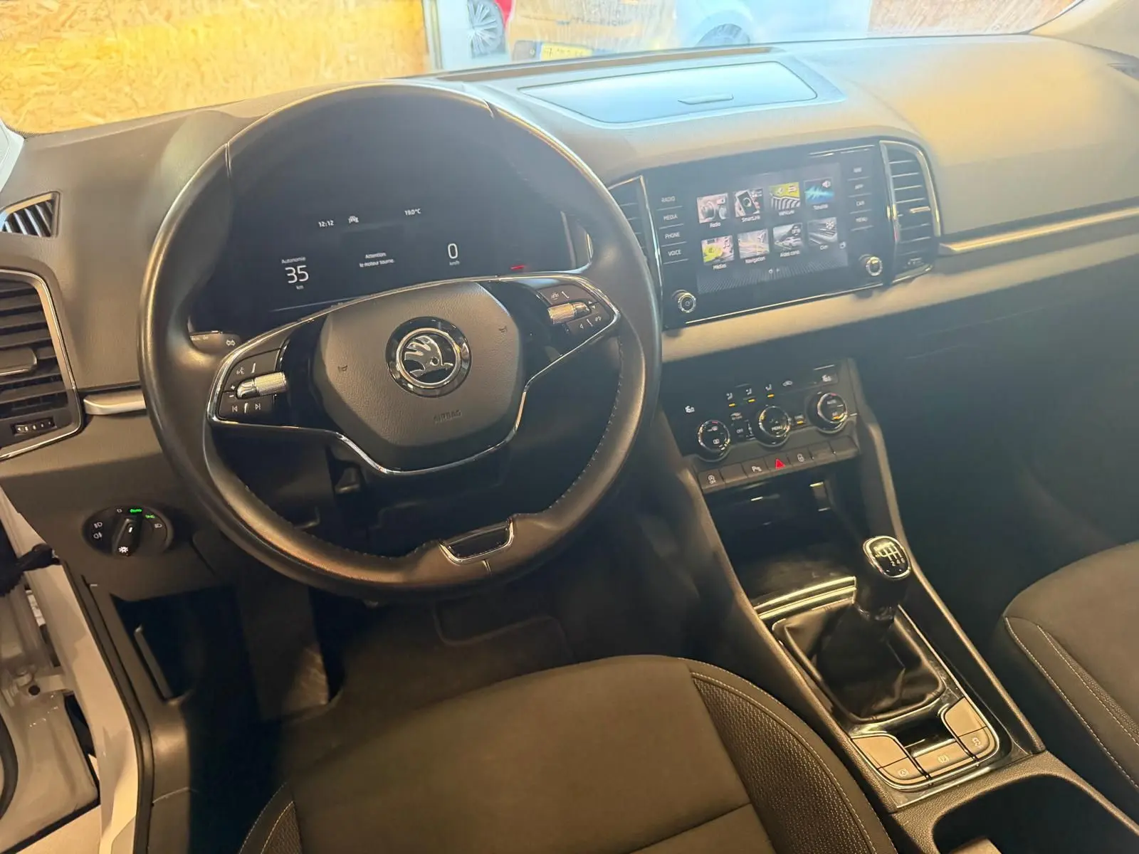 Vue intérieure du poste de conduite du Skoda Karoq blanc 2023, avec volant multifonction et boîte manuelle visible.