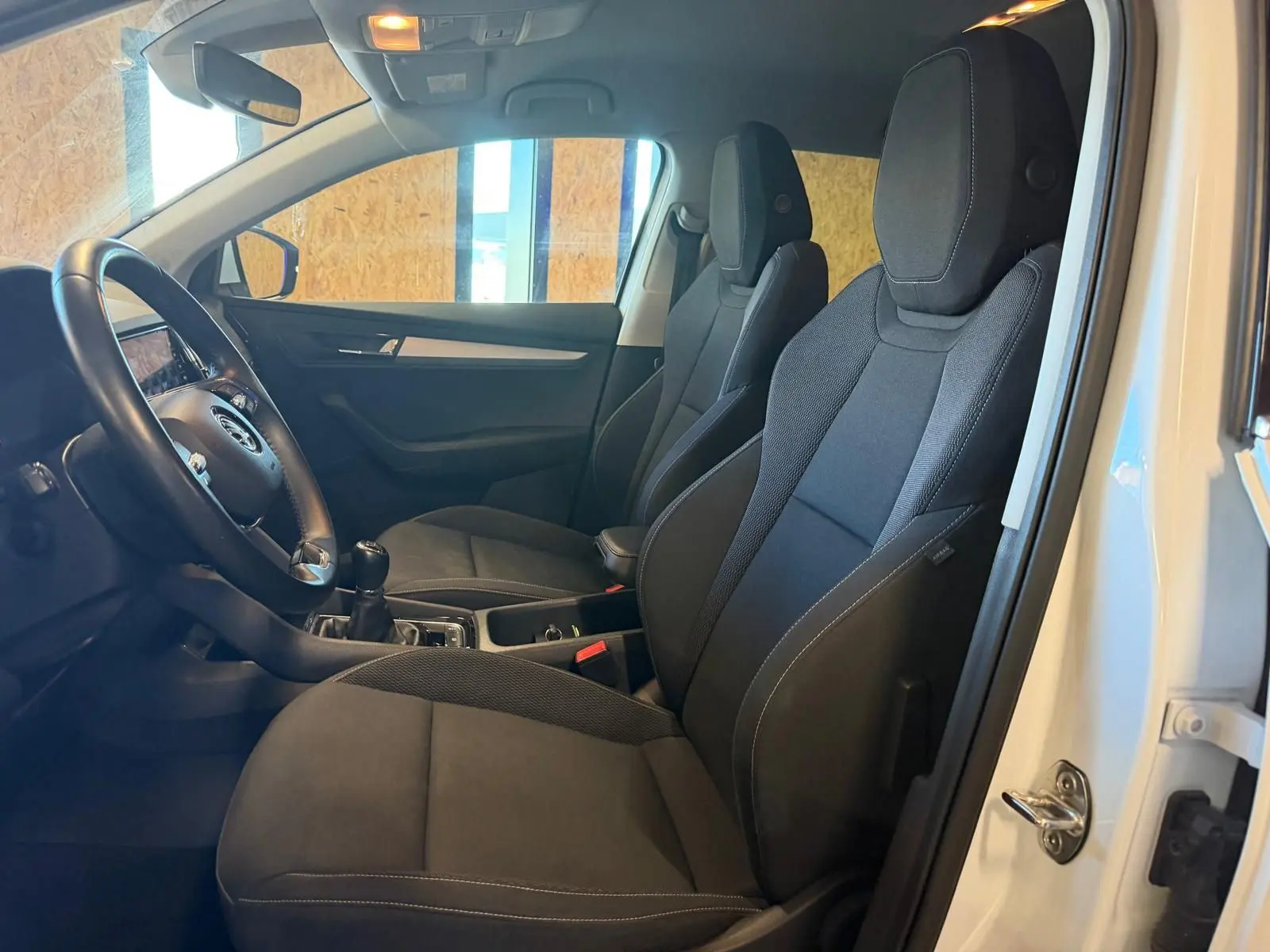 Intérieur du Skoda Karoq 1.5 TSI 2023 en blanc, vue côté conducteur montrant sièges noirs et volant avec boîte manuelle.