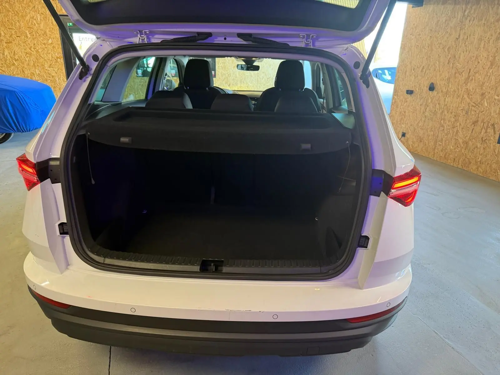Vue arrière d’un Skoda Karoq blanc 2023 avec coffre ouvert, montrant l’espace de chargement et les feux arrière allumés.