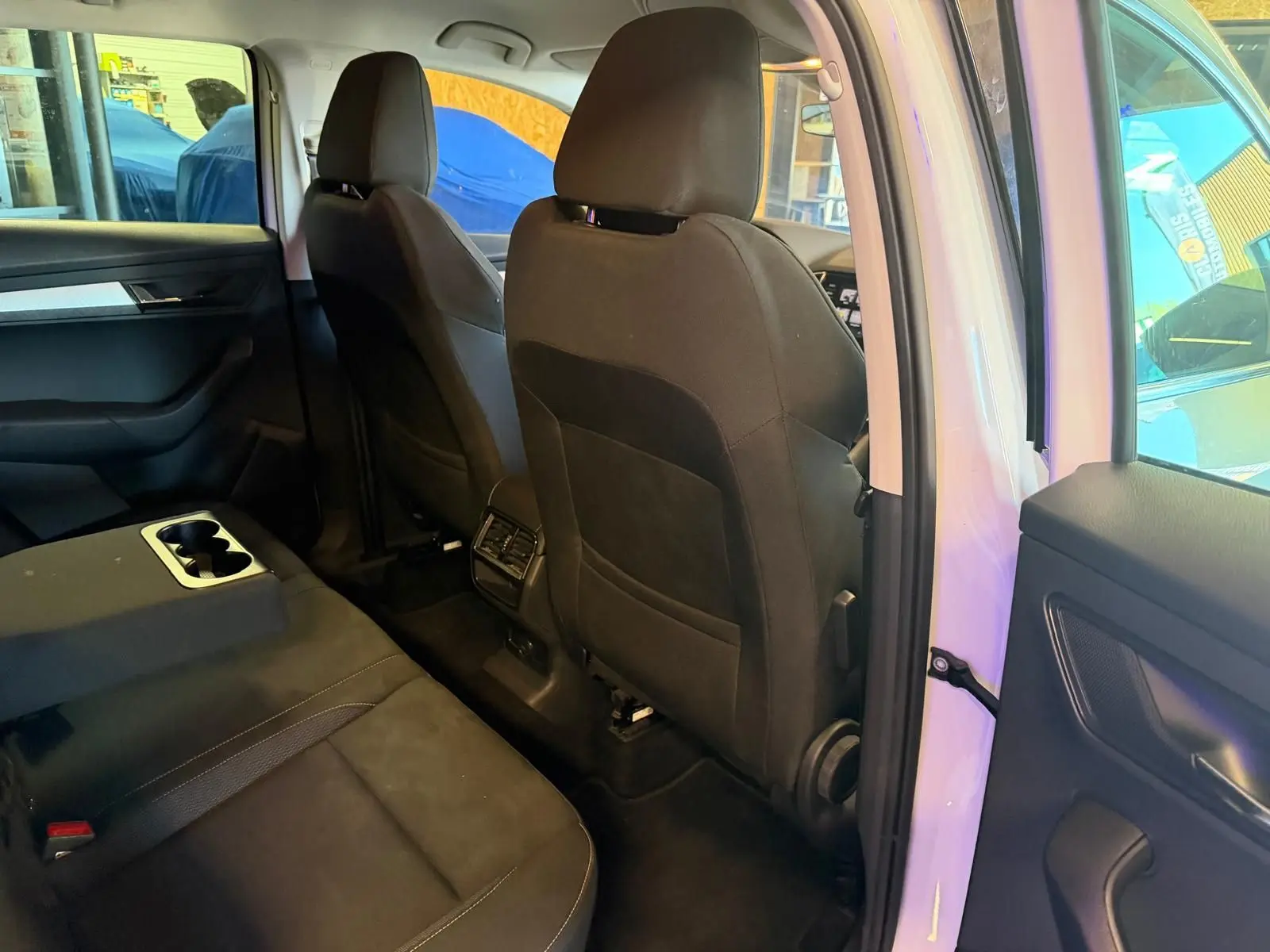 Vue intérieure arrière droite du Skoda Karoq blanc 2023, montrant les sièges noirs et la console centrale avec porte-gobelets.