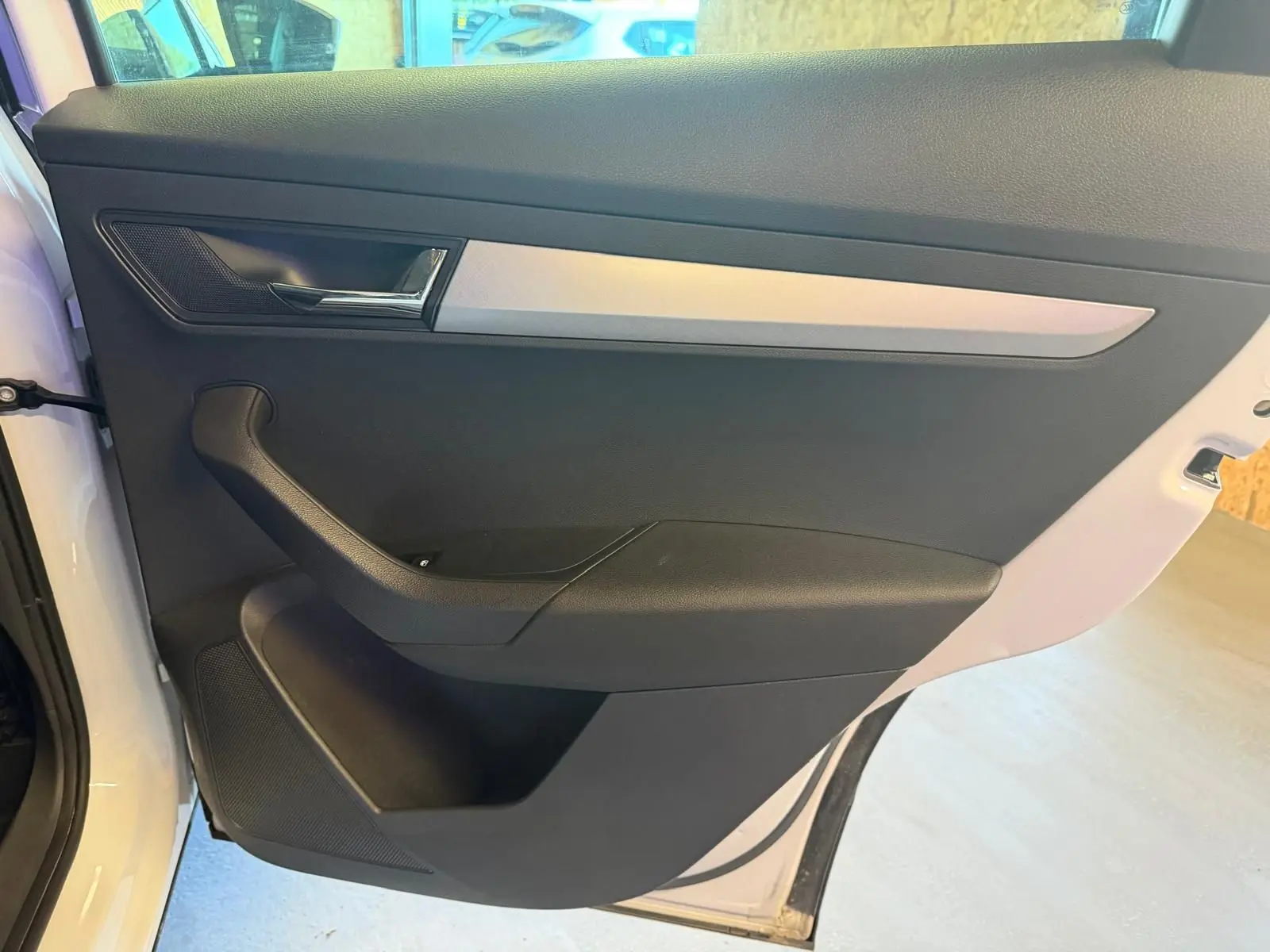 Vue intérieure de la porte avant gauche du Skoda Karoq blanc 2023, avec poignée noire et insert argenté.