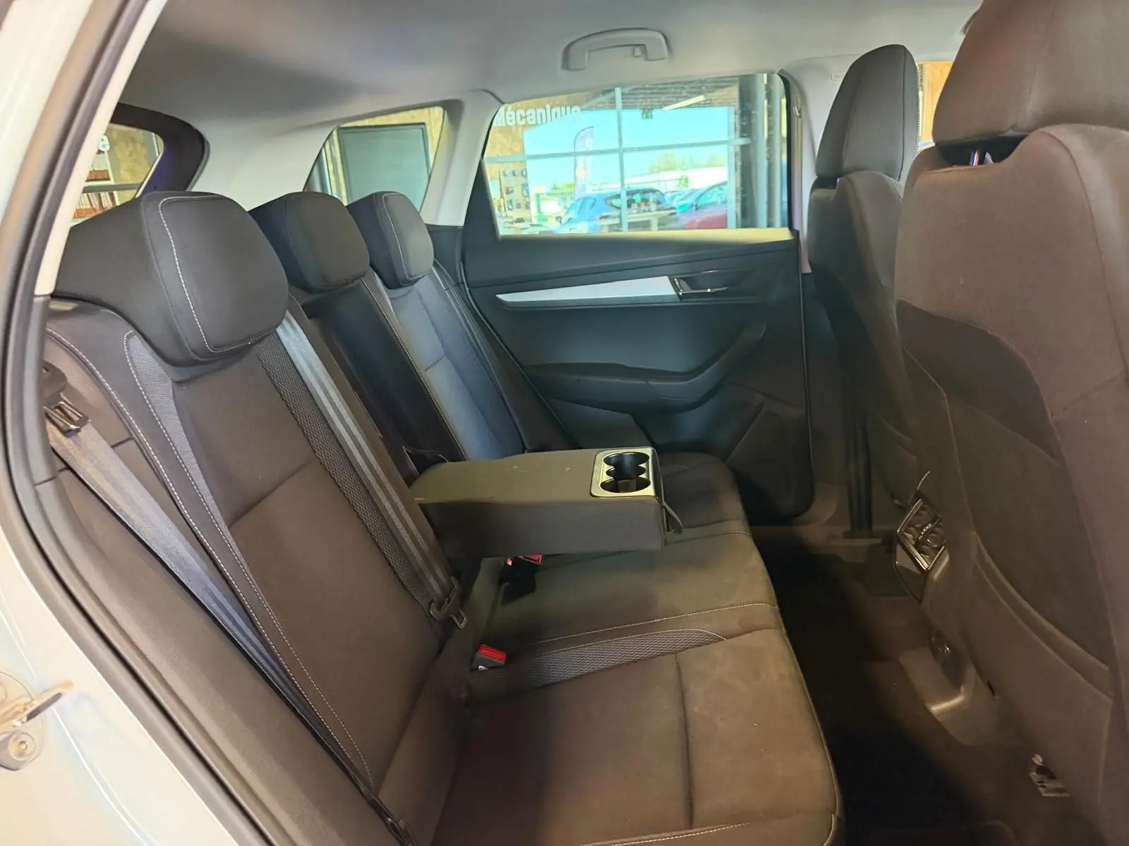 Vue intérieure côté gauche des sièges arrière noirs d'un Skoda Karoq blanc 2023 avec accoudoir central et porte-gobelets.