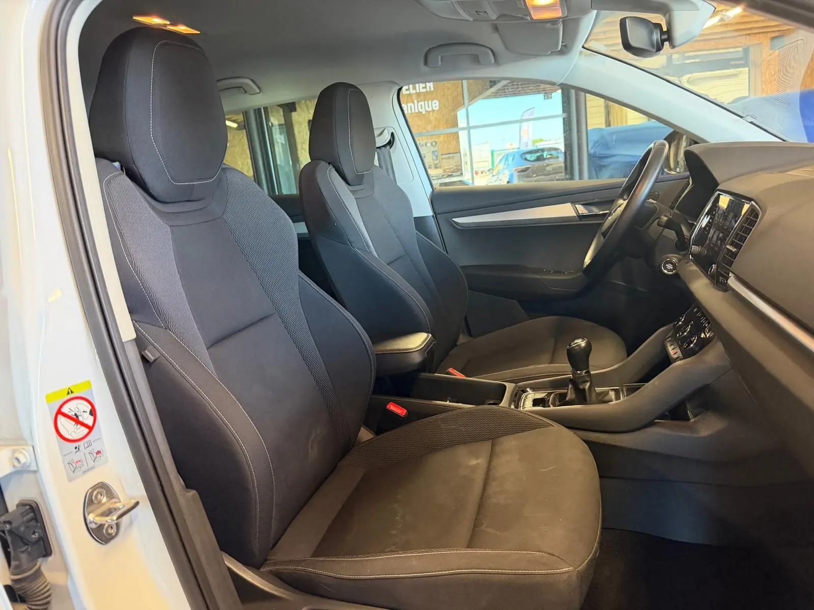 Vue intérieure côté conducteur du Skoda Karoq blanc 2023, montrant les sièges noirs et la boîte manuelle.