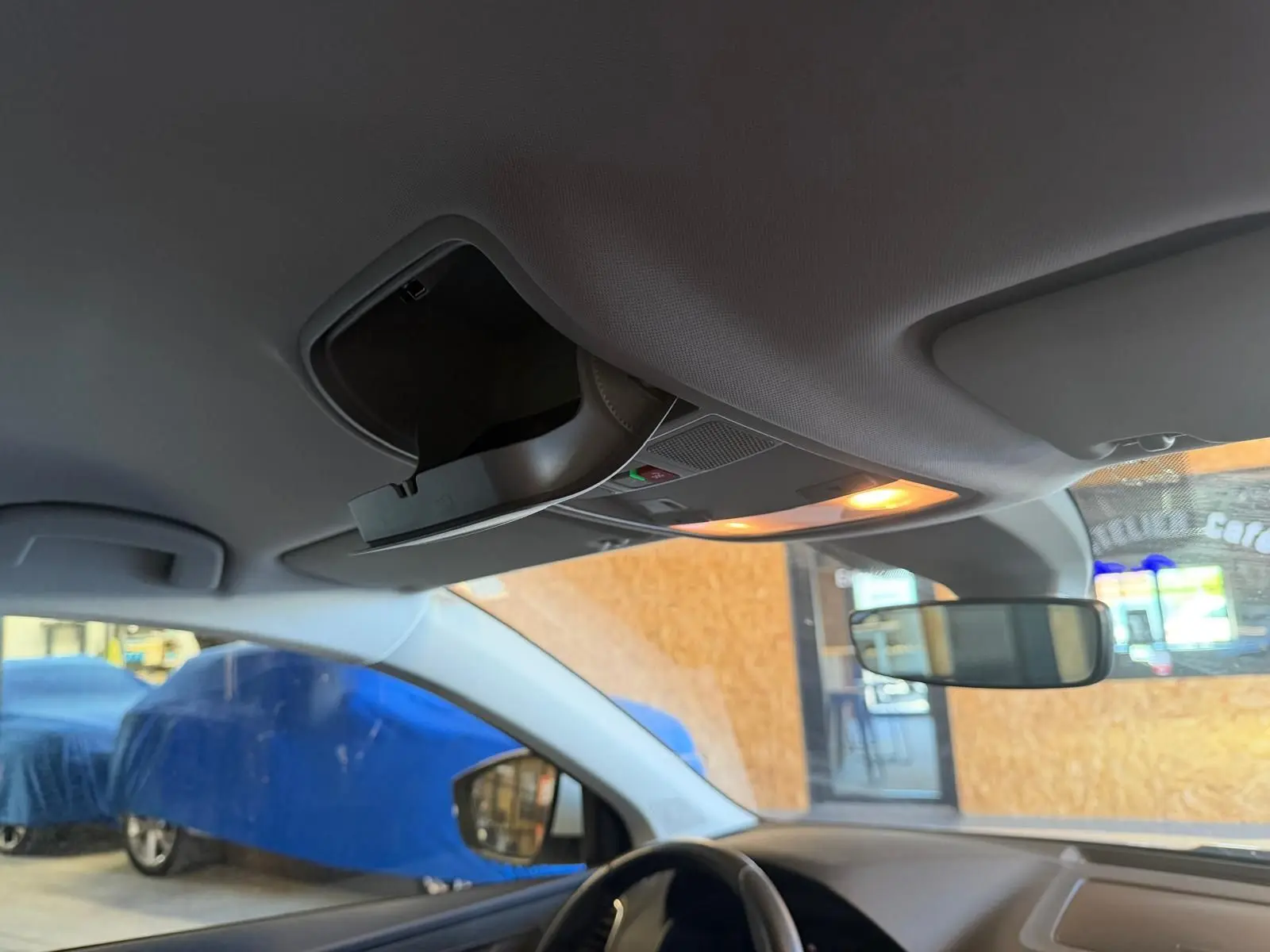 Vue intérieure du plafond avant du Skoda Karoq blanc 2023, montrant le rangement lunettes et l'éclairage intérieur allumé.