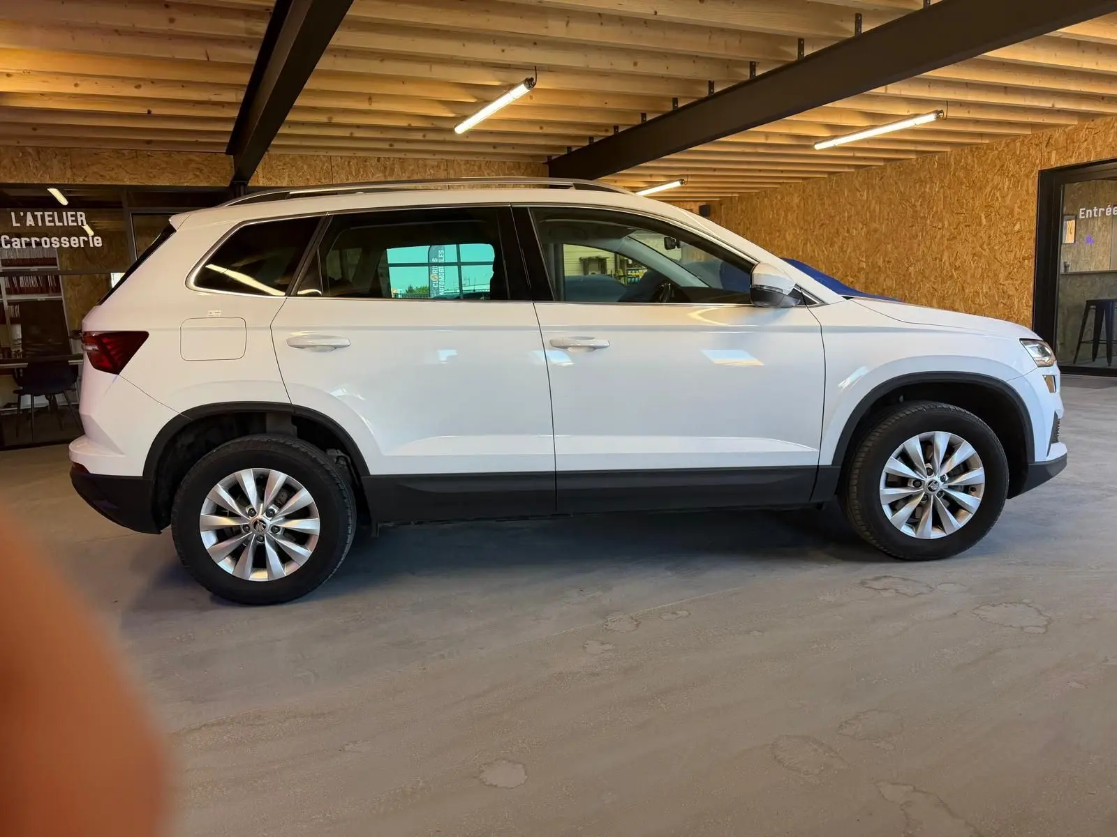Profil droit d’un Skoda Karoq blanc 2023 en version 1.5 TSI Ambition, stationné en intérieur avec jantes alliage visibles.